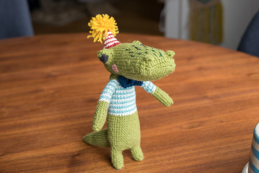 Alligator toy together, wearing a striped shirt and a party hat with a pom
