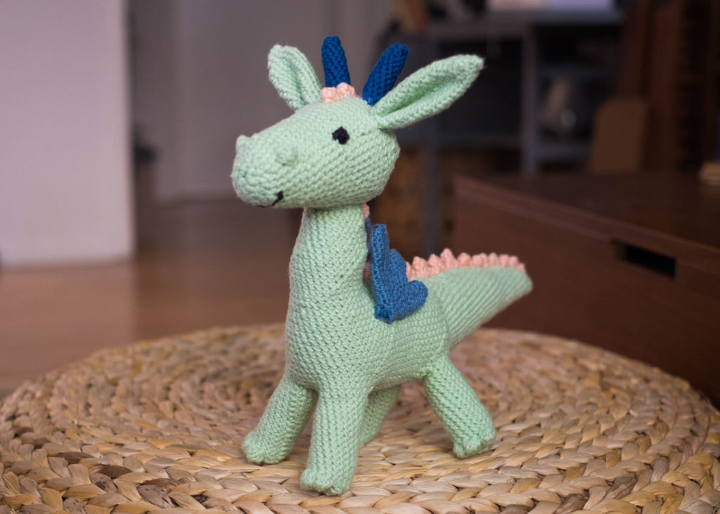 Light green dragon toy with blue wings and horns and pink spikes running down the back