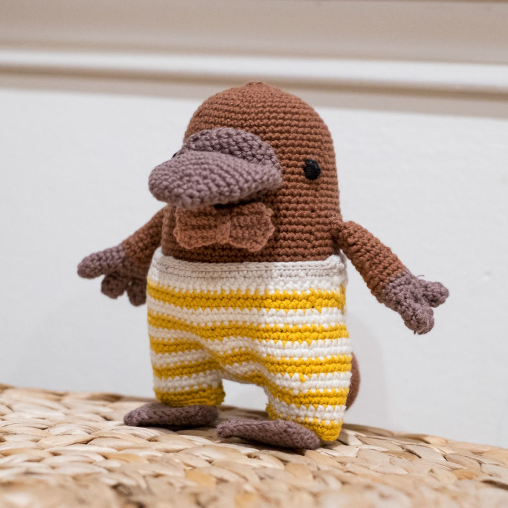squat platypus toy wearing pink bowtie and yellow and white striped pants