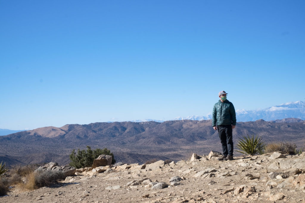 Scott at the top of the mountain. Gray rocky ground with brown and blue mountains in the distance