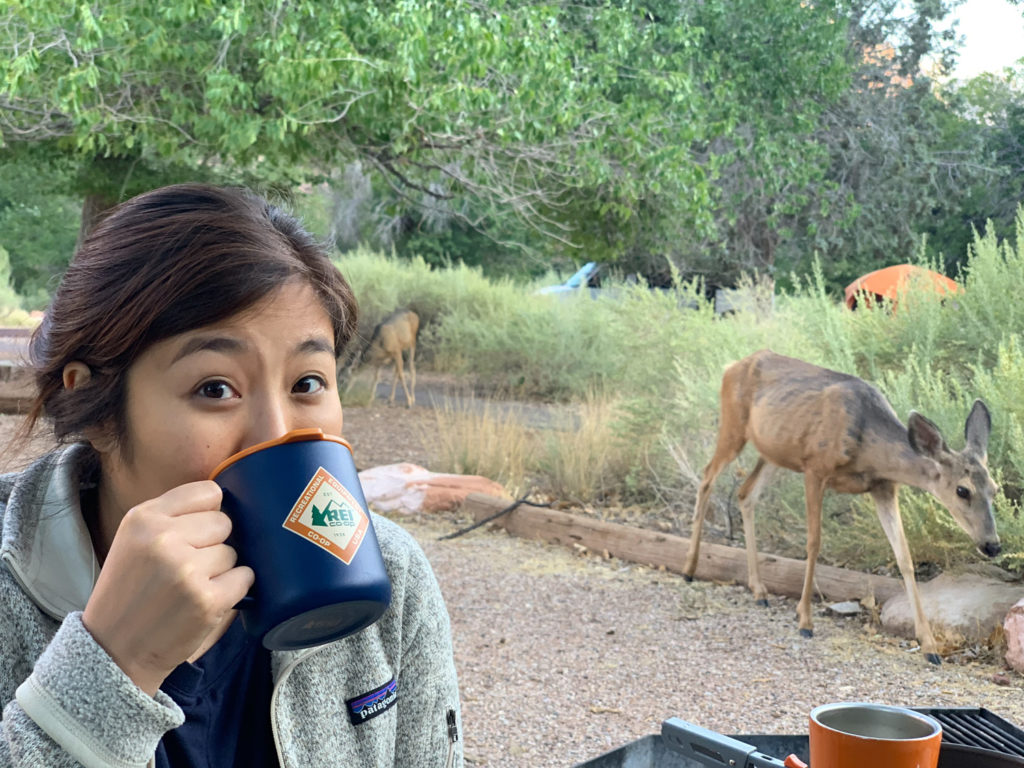 Jack drinking from a mug while two deer are near by in the background
